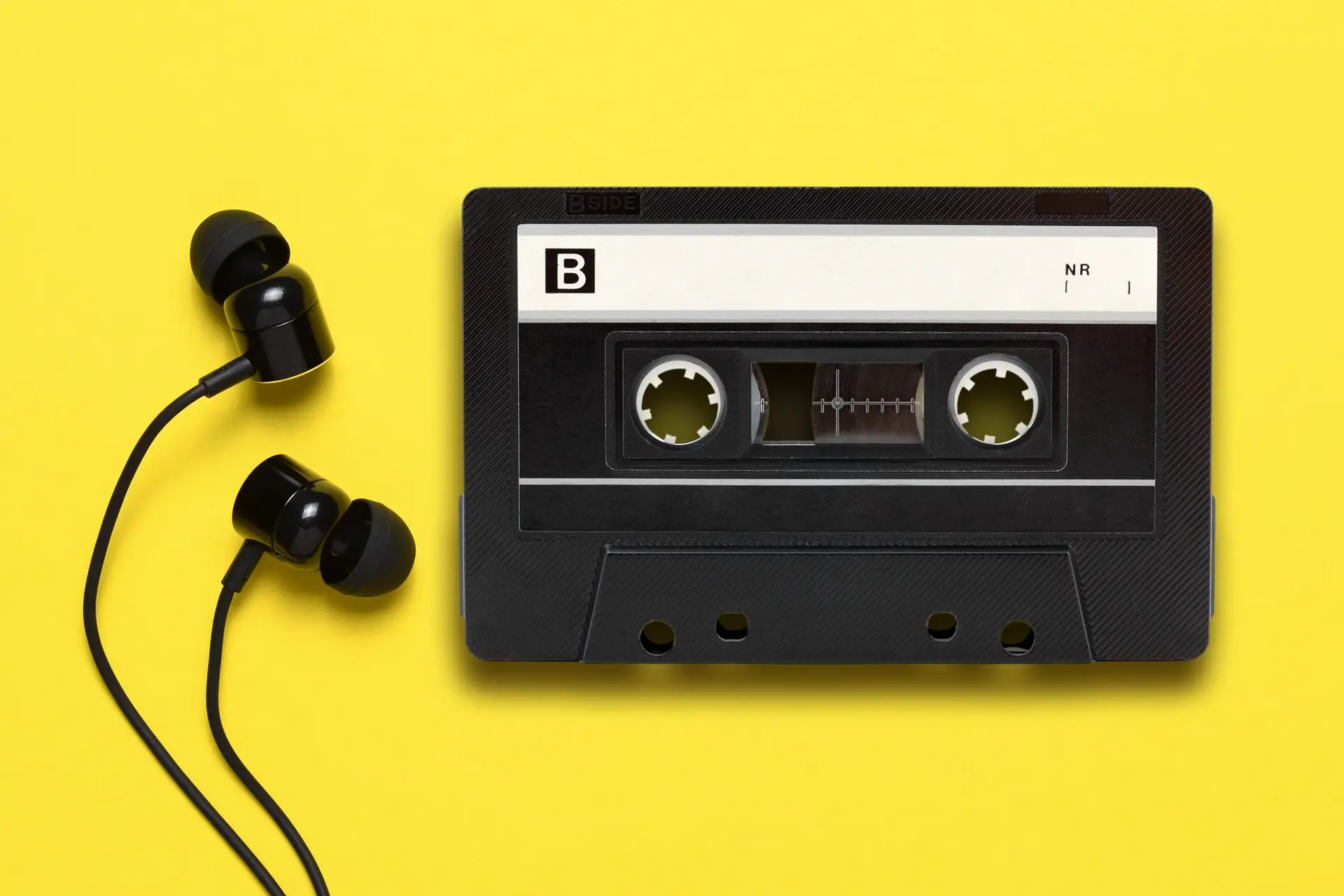 Earphones and audio cassette on yellow background